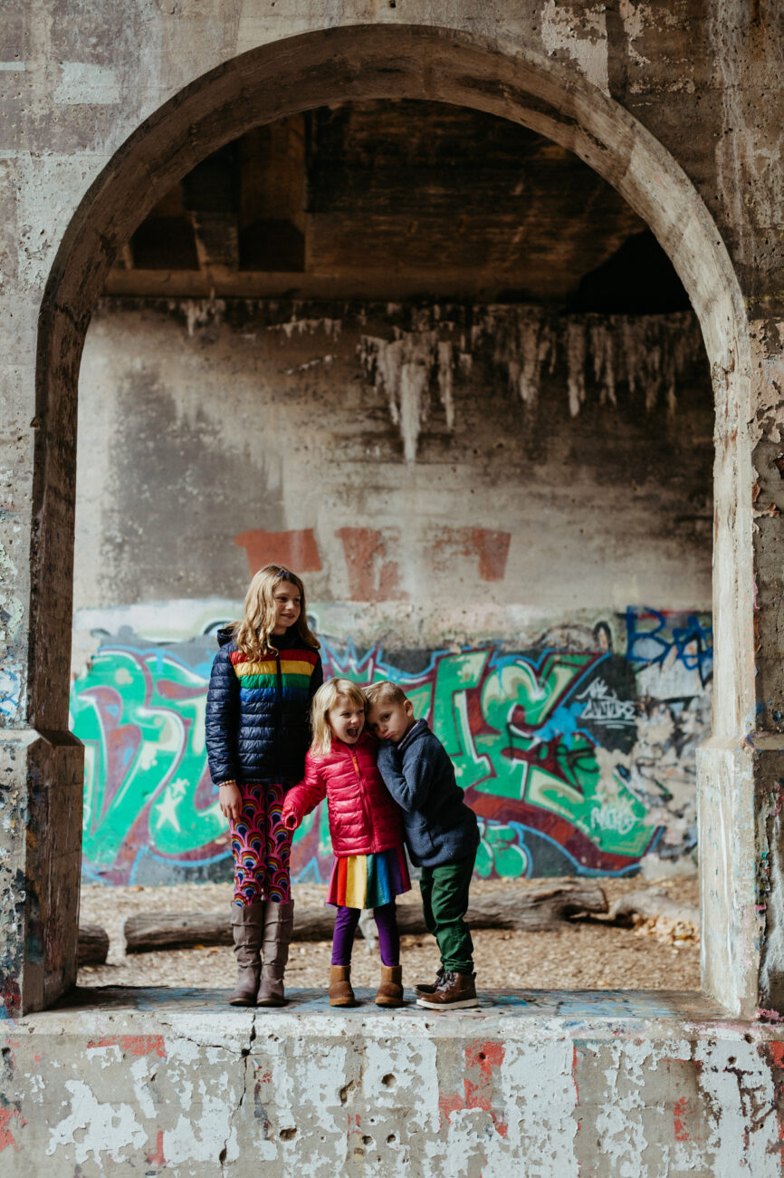 Young siblings posing under freeway arch in front of a wall of graffiti